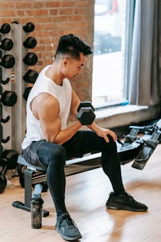 Focused Asian man lifting a dumbbell at an indoor gym, showcasing strength and fitness.