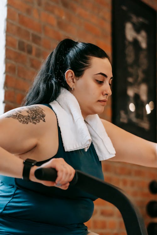 Side view of active plus size ethnic female with towel training on cross trainer machine during workout in modern gym