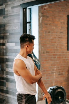 Muscular Asian man in a modern gym, reflecting on his workout journey. Fitness lifestyle.