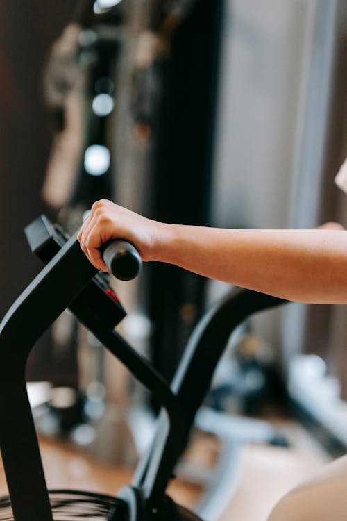 Free Unrecognizable sportive person training on modern cross trainer machine while working out in spacious gym with special equipment on blurred background Stock Photo