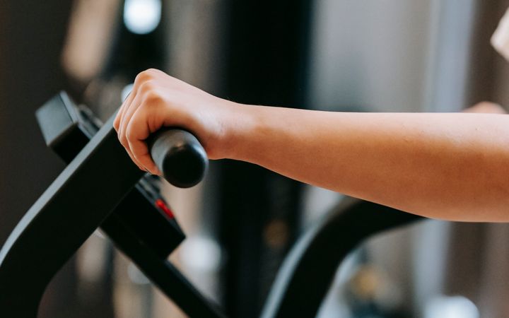 Unrecognizable sportive person training on modern cross trainer machine while working out in spacious gym with special equipment on blurred background