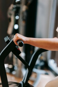 Unrecognizable sportive person training on modern cross trainer machine while working out in spacious gym with special equipment on blurred background