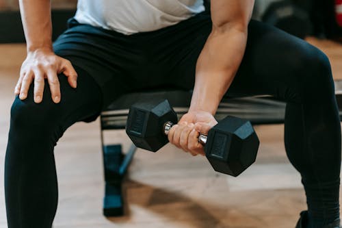 Crop man lifting dumbbell on bench