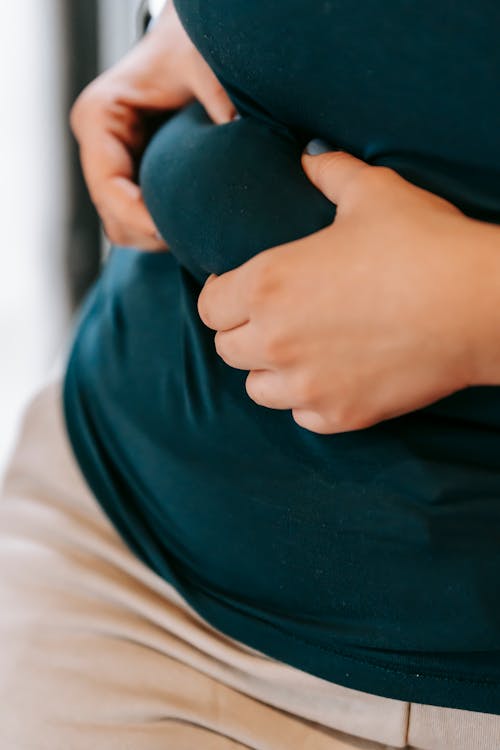 Unrecognizable plus size female in activewear touching folds on belly while standing on blurred background during training in light gym