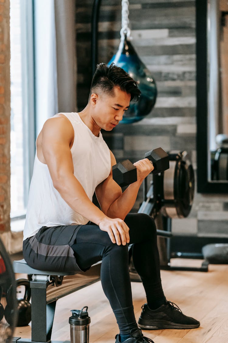 Fit Asian Man Exercising With Dumbbell In Gym