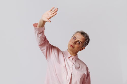 Portrait of a stylish woman in a pink shirt posing against a white background, hand raised.