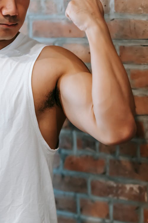 Free Crop anonymous sporty fit male demonstrating strong arm with bicep near brick wall Stock Photo