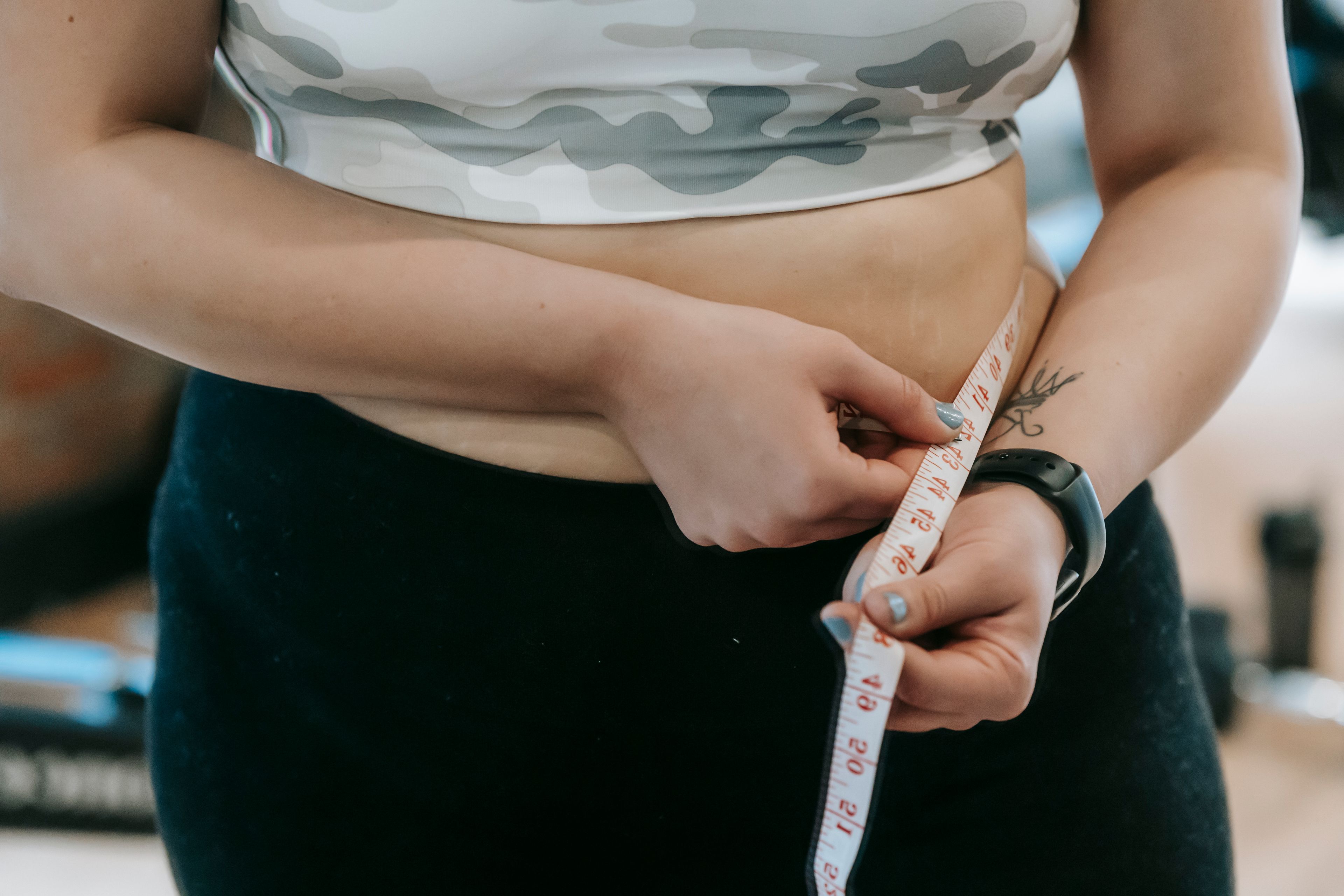 Crop anonymous plus size female with measuring tape measuring waist on blurred background