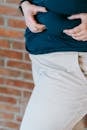 Crop unrecognizable plump female showing big belly on blurred background of brick wall