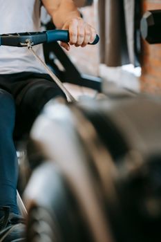 Crop anonymous sporty strong male exercising on modern rowing machine in sport club