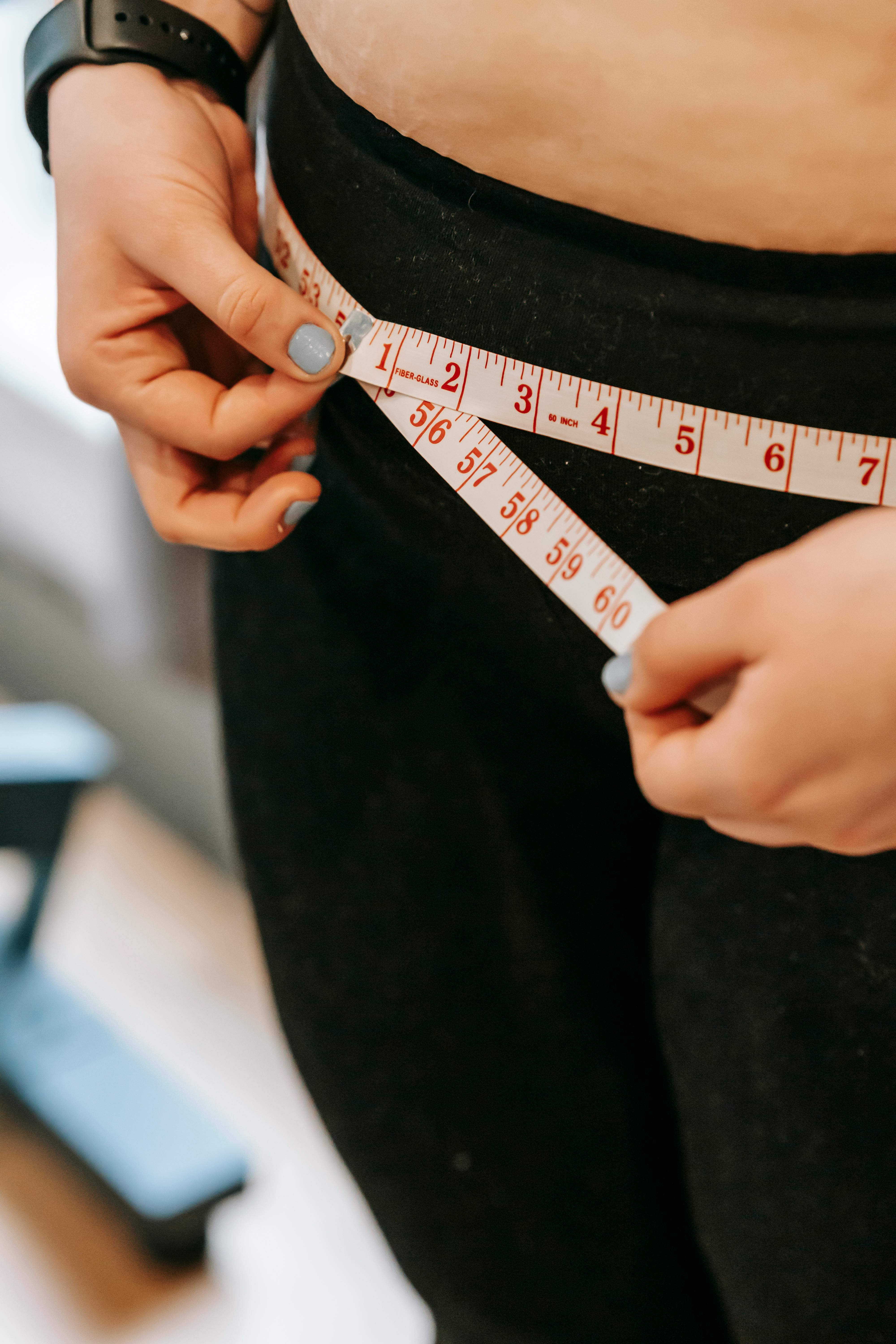 Free From above of crop anonymous plump female using measuring tape around hips in gym Stock Photo