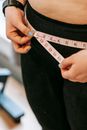 From above of crop anonymous plump female using measuring tape around hips in gym