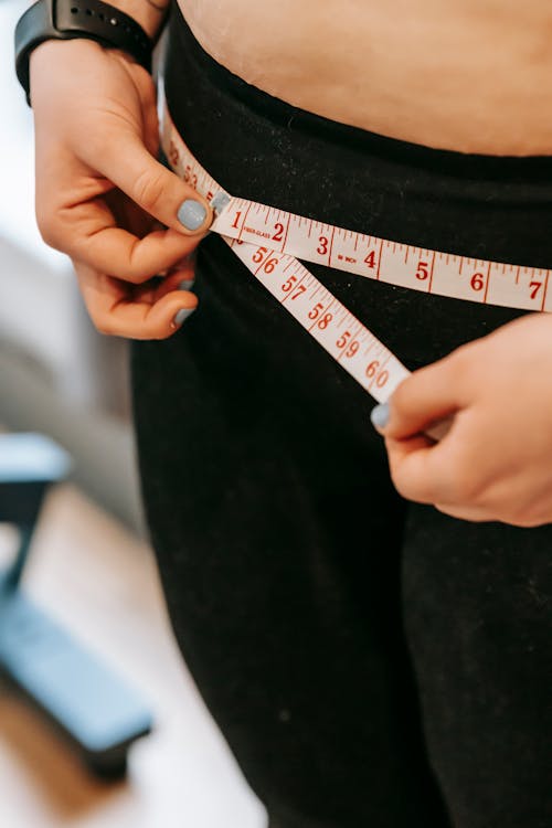 Free From above of crop anonymous plump female using measuring tape around hips in gym Stock Photo