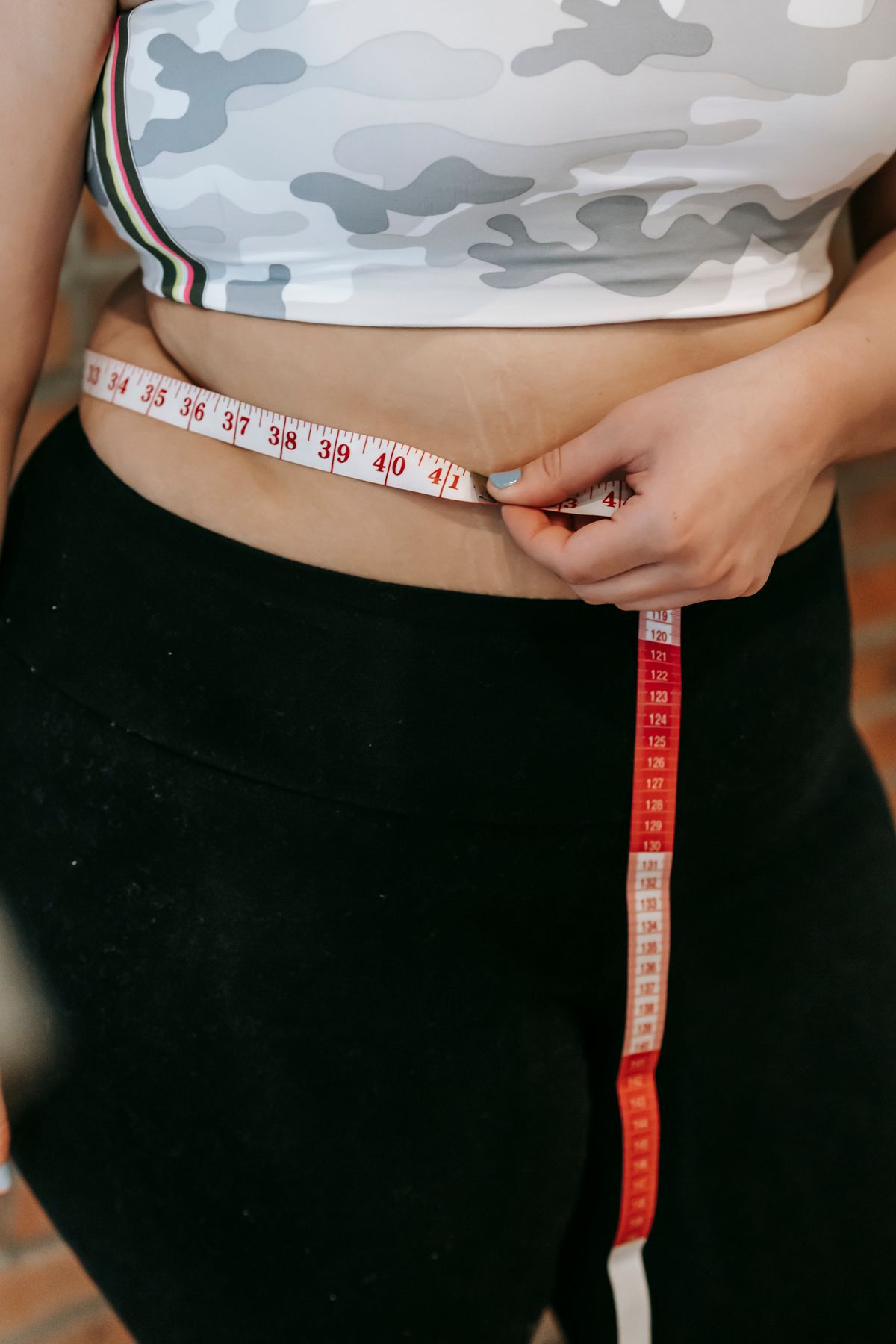 Woman measuring her waist with a tape measure while wearing activewear