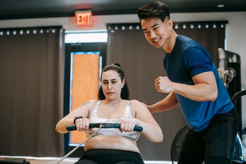 Free Happy ethnic young instructor supporting plus size woman working out on rowing machine in sport club Stock Photo