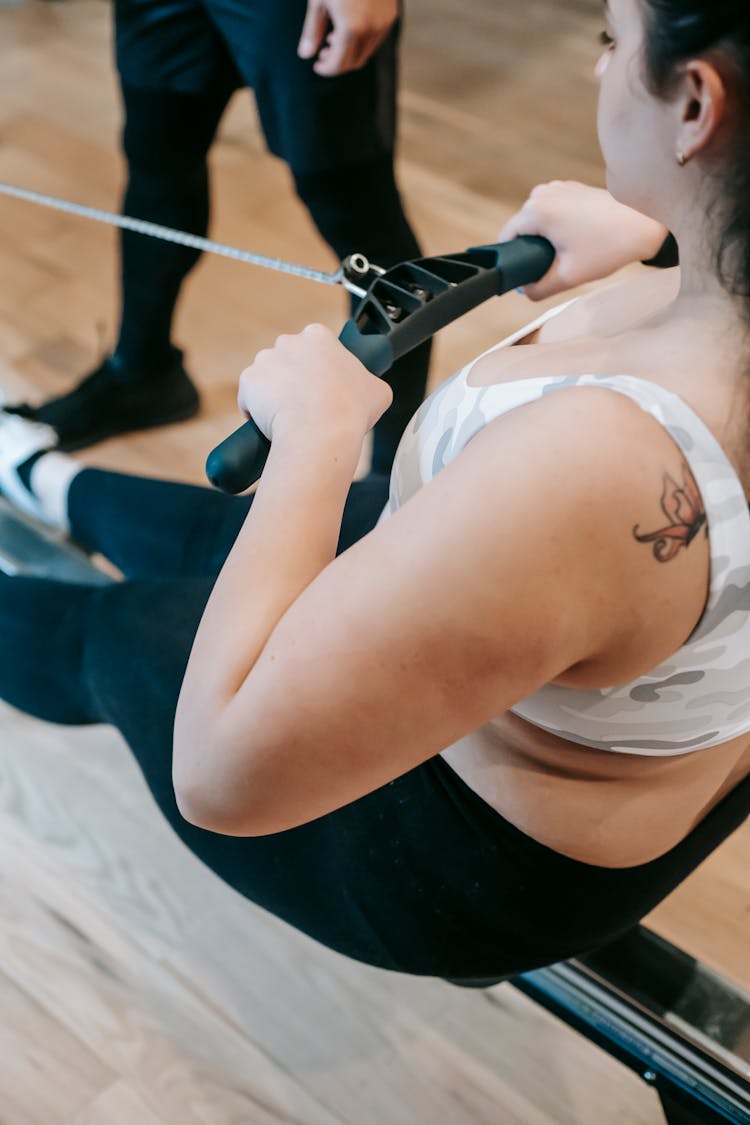 Plus Size Woman Doing Pulling Exercise In Gym Near Anonymous Coach