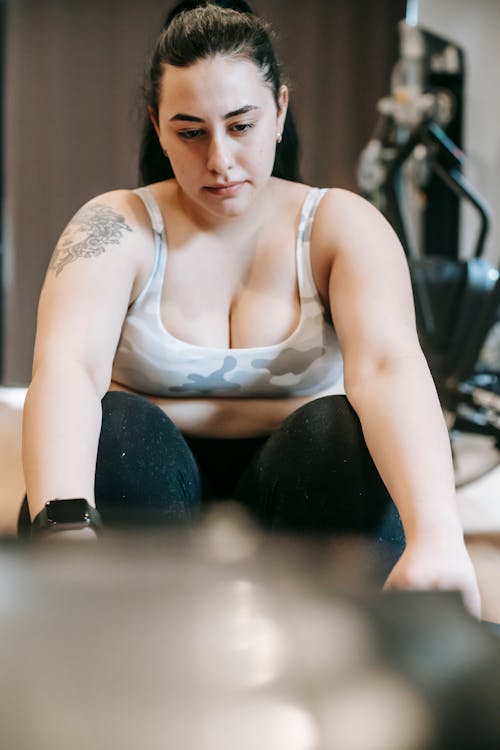 Tired young tattooed plus size female with long dark hair in sportswear resting in modern gym during intense workout