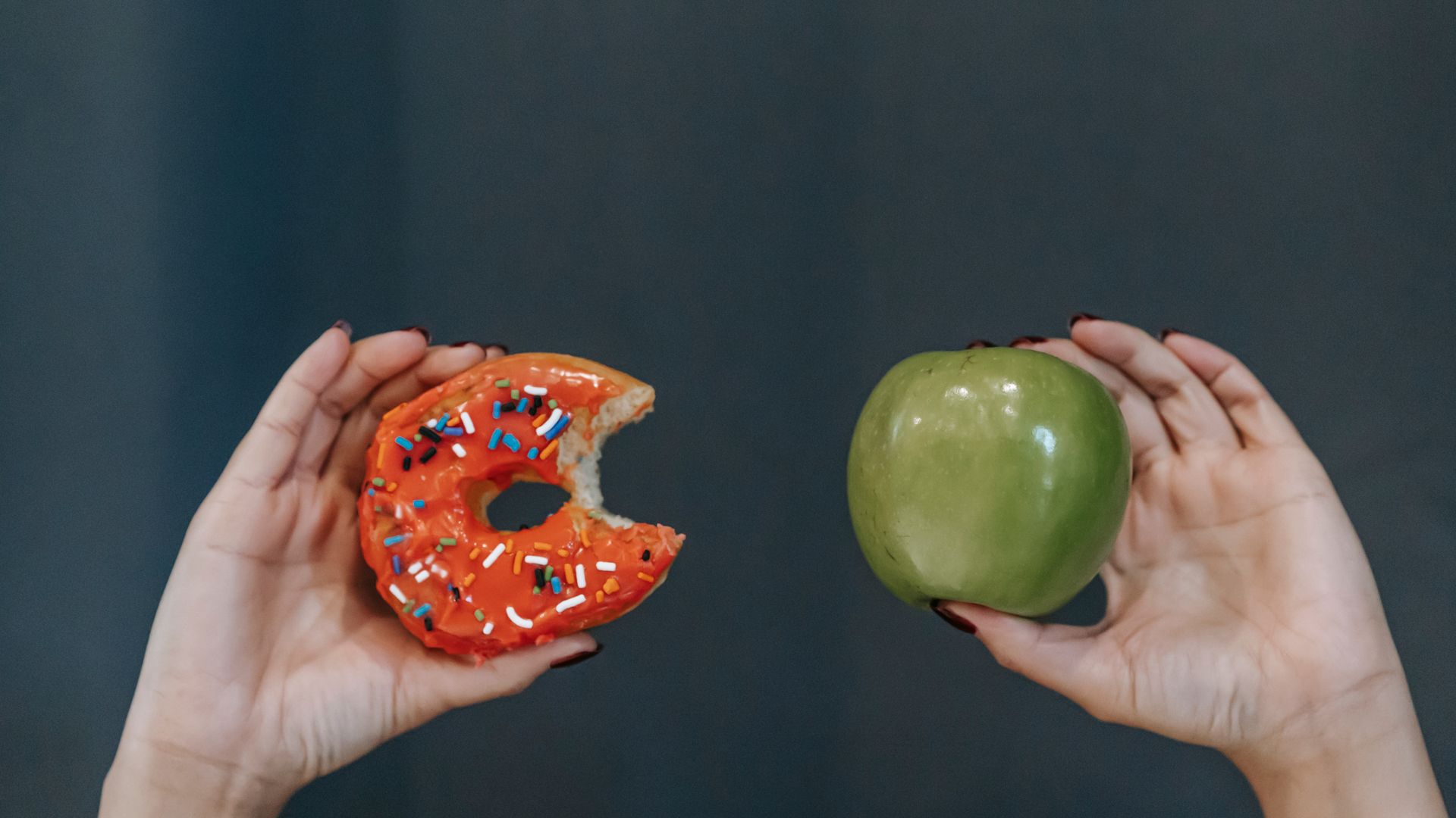 Adrafinil vs Modafinil: Unlocking the Differences Crop unrecognizable young female demonstrating bitten high calorie doughnut and healthy green apple against gray background — adrafinil vs modafinil