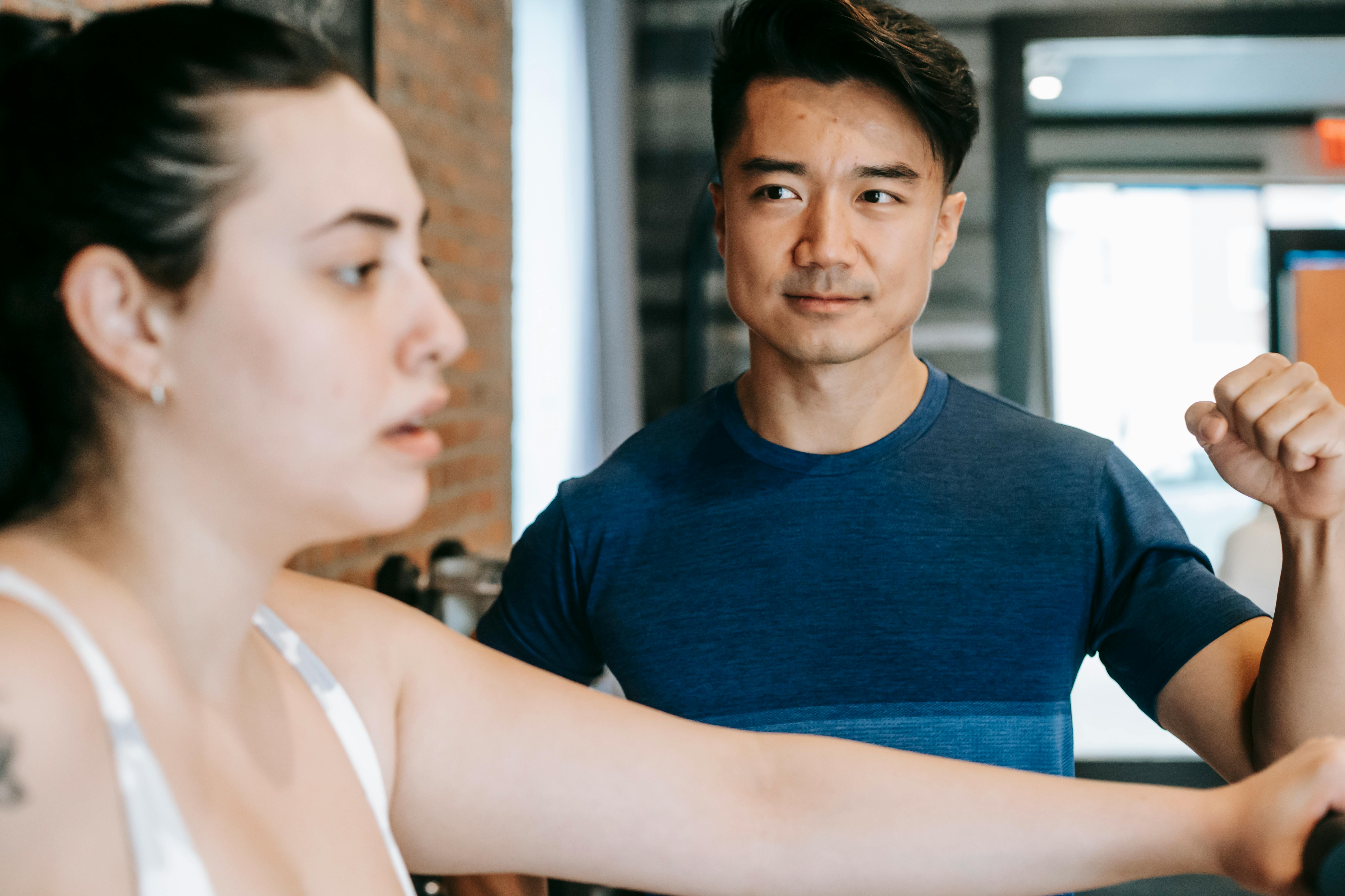 young ethnic male coach motivating overweight woman training in club