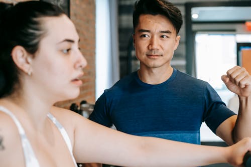 Young ethnic male coach motivating overweight woman training in club