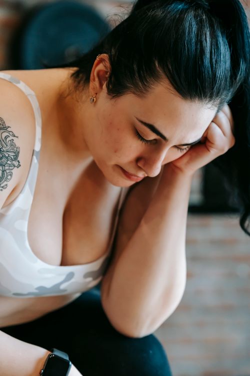 Free Calm young plus size tattooed female with dark hair in sportive top and leggings leaning on hand while resting after hard training in gym Stock Photo