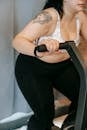 Side view of crop unrecognizable tattooed plus size lady in activewear exercising on cycling equipment during weigh lose workout in gym