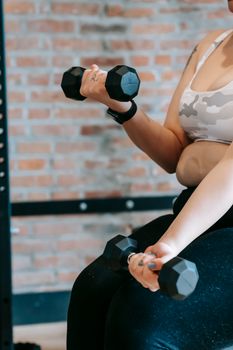 Side view of crop anonymous plus size woman in activewear lifting dumbbells during weight lose training in modern sports center