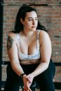 Pensive young plus size woman resting on bench in sports club