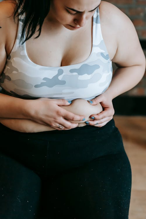 Focused young overweight woman touching stomach in gym