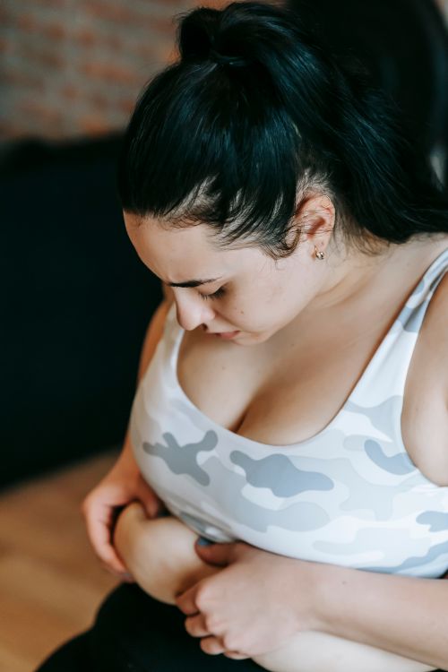Free High angle of thoughtful young overweight lady with long dark hair in sportswear touching belly fat while sitting on bench in gym after training Stock Photo