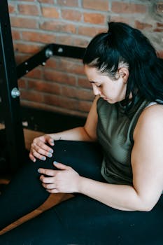 Woman in activewear looking down, taking a break from workout in gym.