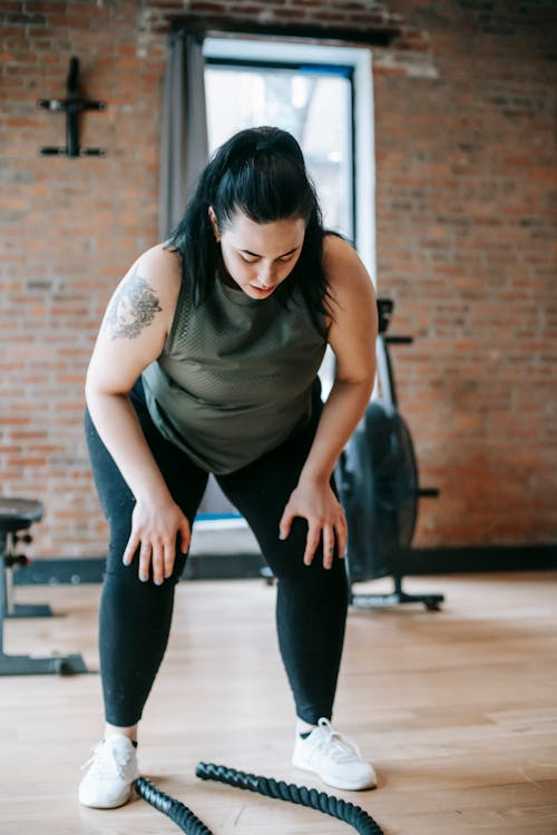 Tired woman leaning on knees during training with battle ropes