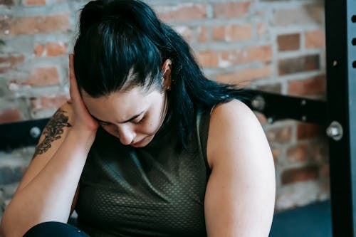 Upset female sitting near sports equipment and feeling desperate and hopeless at training in fitness club