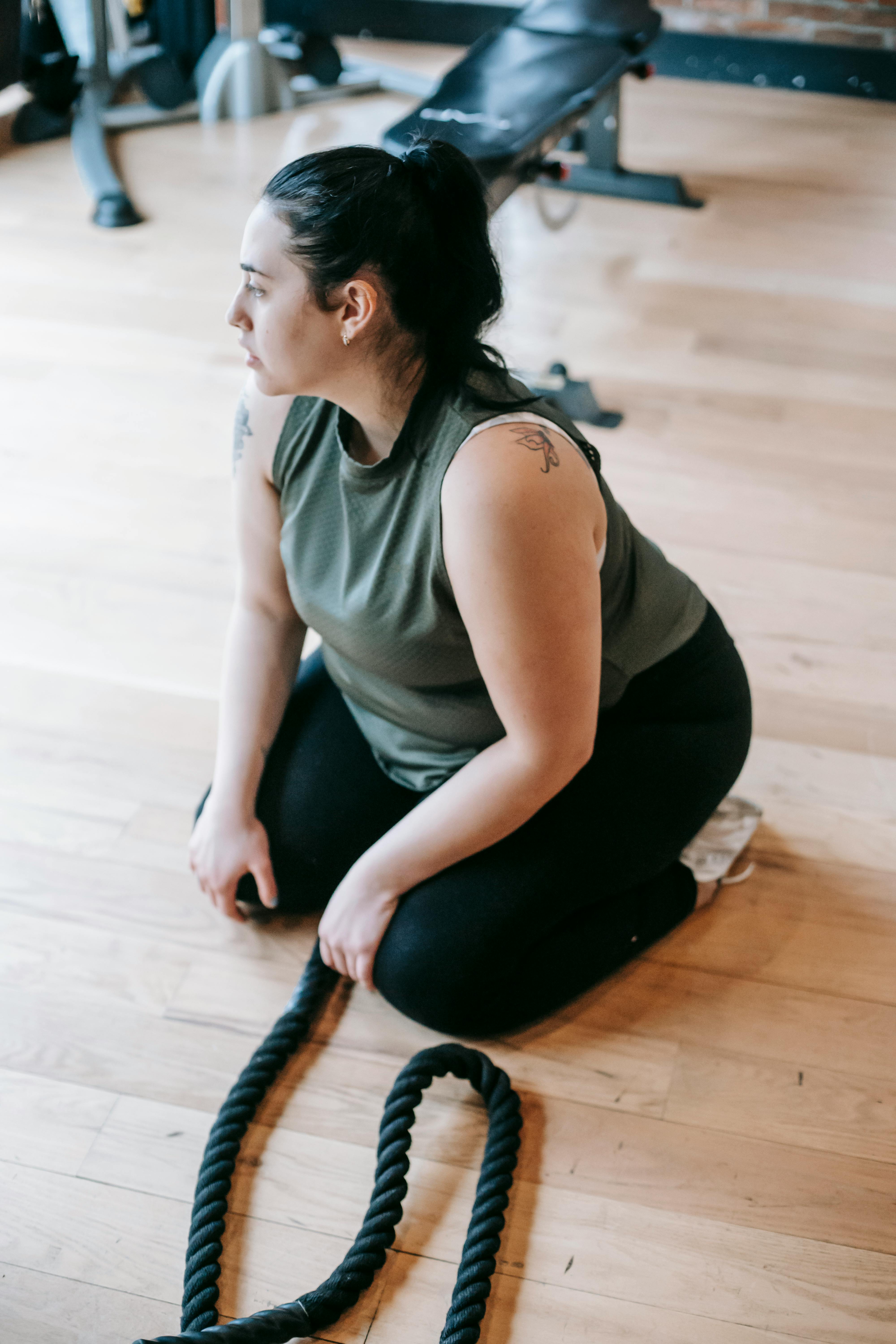 overweight woman sitting on floor in gym near battle ropes