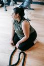 Overweight woman sitting on floor in gym near battle ropes