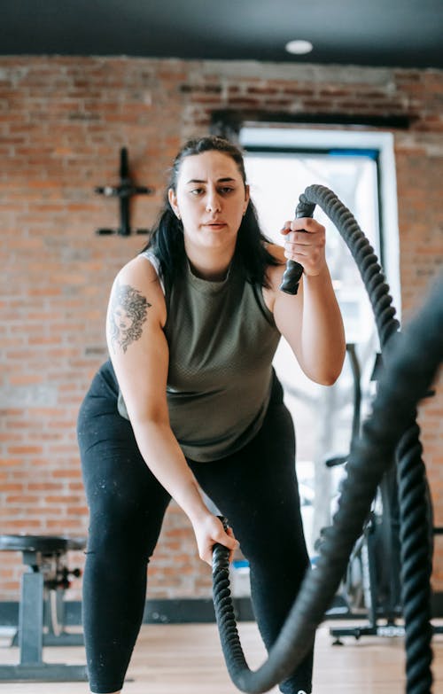 Low angle of concentrated female in sportswear exercising with heavy battle ropes during intense functional training