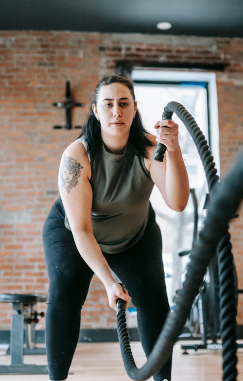 Free Low angle of concentrated female in sportswear exercising with heavy battle ropes during intense functional training Stock Photo