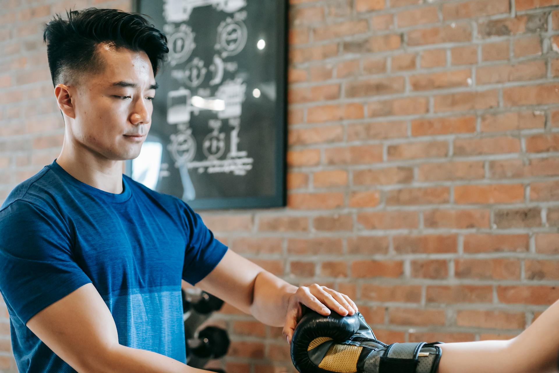 Serious Asian trainer putting on woman gloves before workout