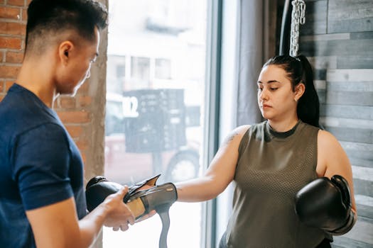 Professional personal trainer preparing focused woman for boxing training while putting on gloves in gym