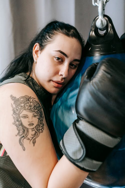 Side view of tired female with tattoo having break in boxing training in gym and looking at camera