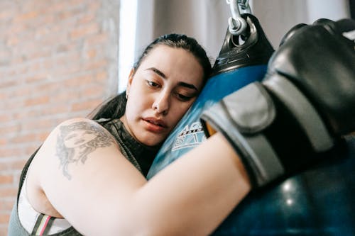 Low angle side view of exhausted young female in boxing gloves having pause in hard training in fitness center