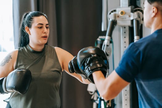 Focused female boxer practicing punches with male coach using mitts in a gym setting.