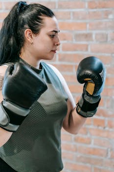 Side view of enduring woman wearing sportswear and boxing gloves standing in gym during workout