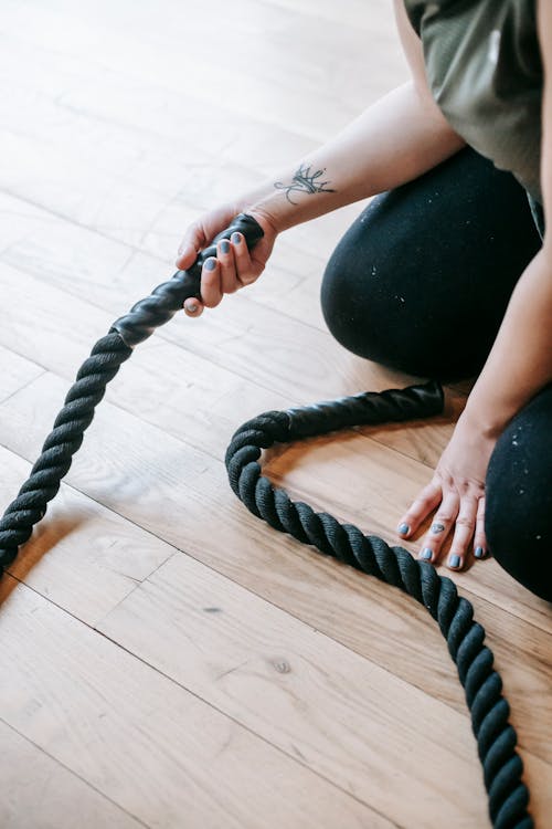 Free High angle of crop anonymous woman with battle rope resting on floor after intense training Stock Photo