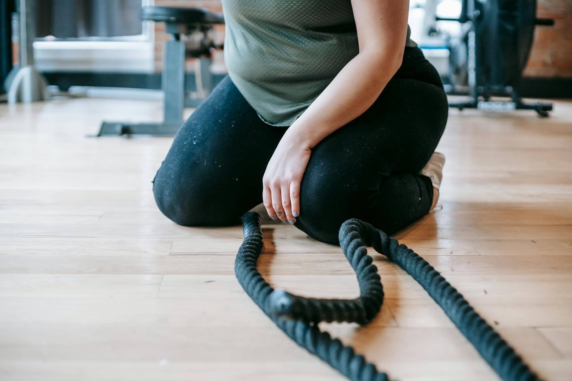 Crop unrecognizable female in sportswear sitting on floor near sports equipment during weight loss workout