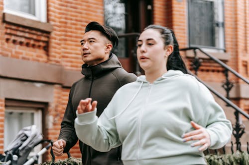 Determined young obese woman with male Asian personal trainer jogging on street