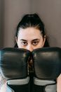 Powerful young sportswoman with long dark hair demonstrating fists in boxing gloves and looking at camera during workout