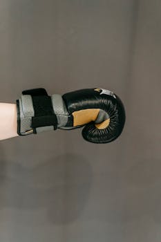 Side view of crop anonymous person in boxing gloves punching against gray background during workout