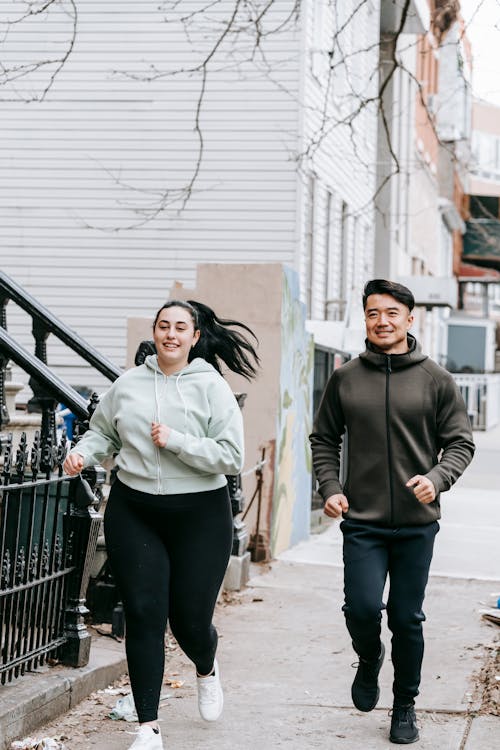 Happy fit ethnic man and obese woman jogging together on city street