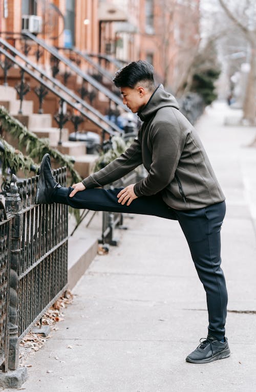 Free Sporty young ethnic guy stretching leg on street after jogging Stock Photo